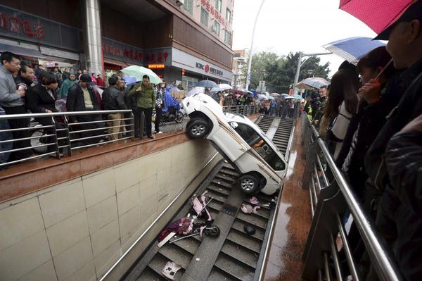 People look on as a car is stuck after falling into a stairs of an underpass, in Fuzhou, Fujian province, China, December 9, 2015. The driver, surnamed Yang, in her 30s, backed the car into the underpass entrance on Wednesday by mistaking the accelerator as the brake. No one was injured during the accident, local media reported. Picture taken December 9, 2015. REUTERS/Stringer
